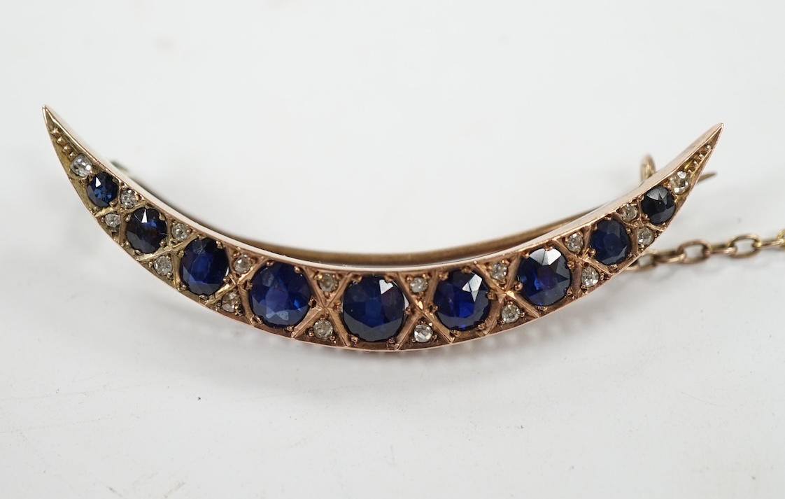 An early 20th century yellow metal, graduated sapphire set crescent brooch, with diamond chip spacers, 49mm, gross weight 5.8 grams. Condition - fair to good